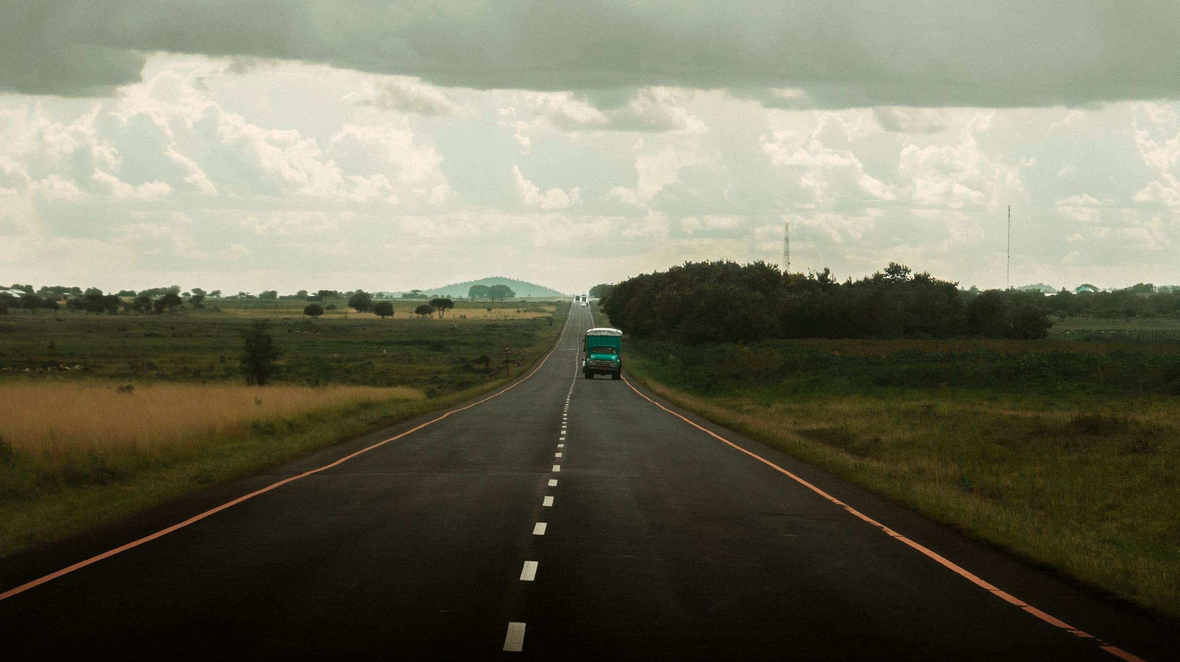 Un camion seul sur une longue route droite traversant la savane, sous un ciel chargé.