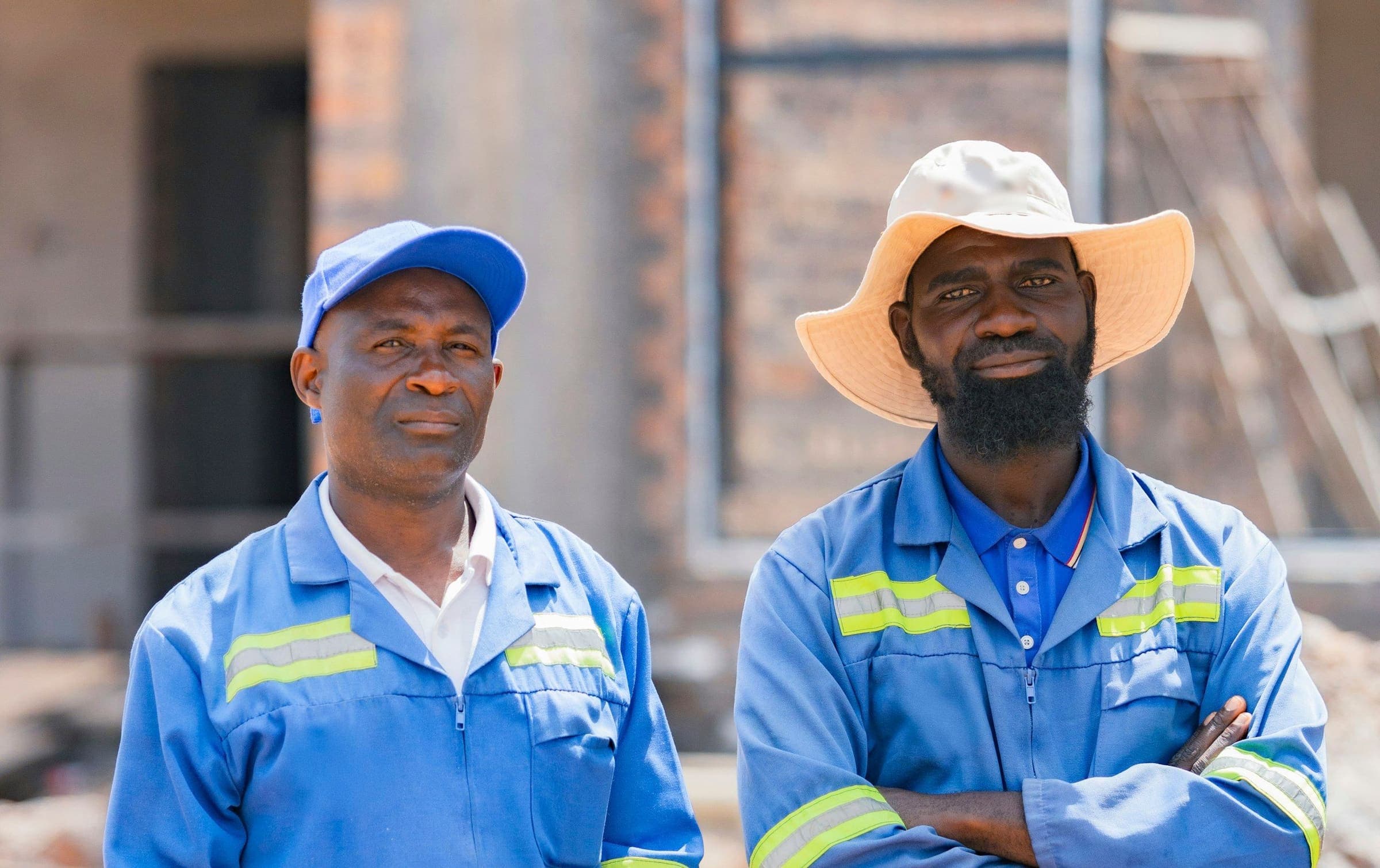 Deux ouvriers de chantier expérimentés en salopette bleue, devant un bâtiment en construction.