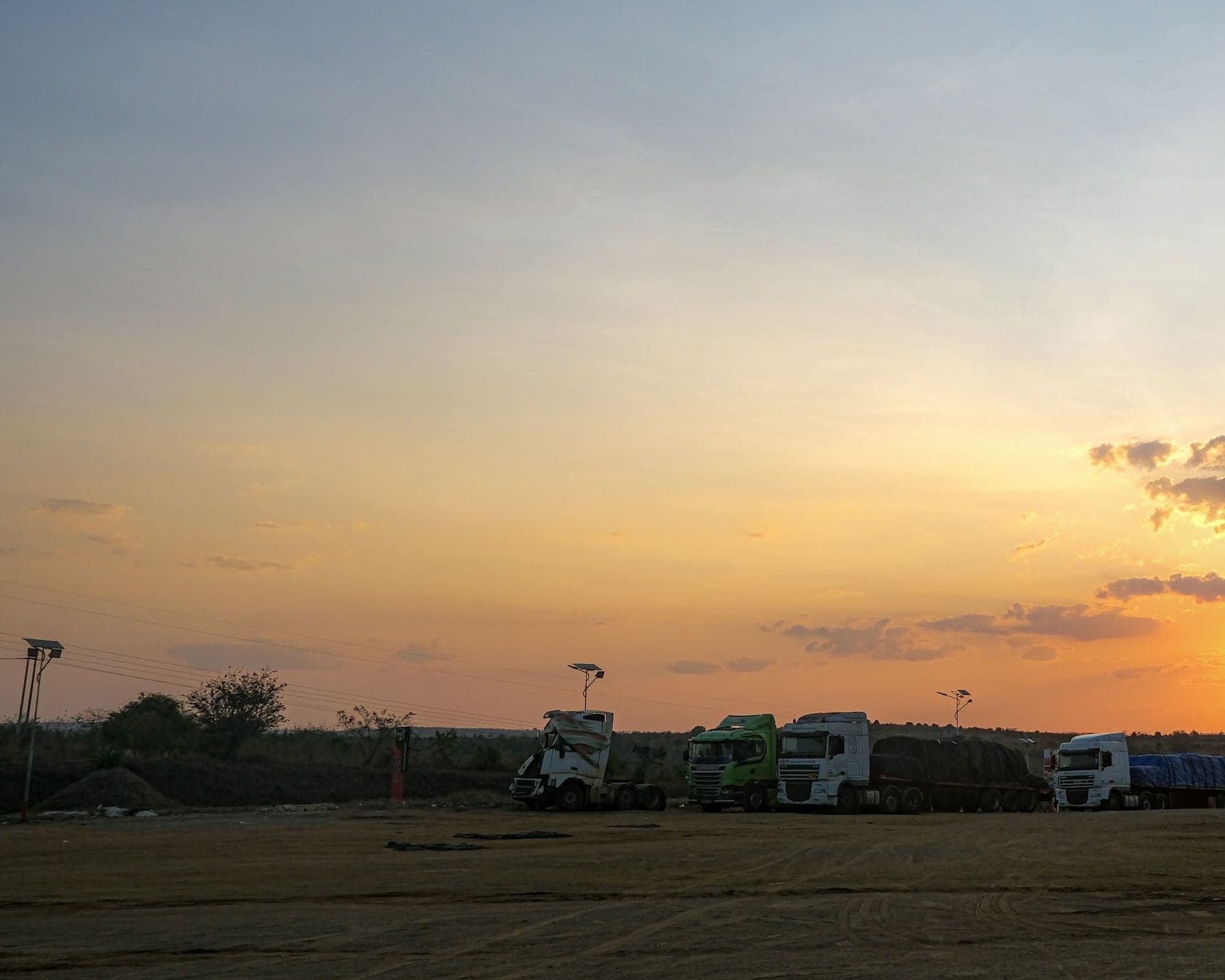 Camions longue distance stationnés sur une aire de repos, sous un ciel orangé au coucher du soleil.
