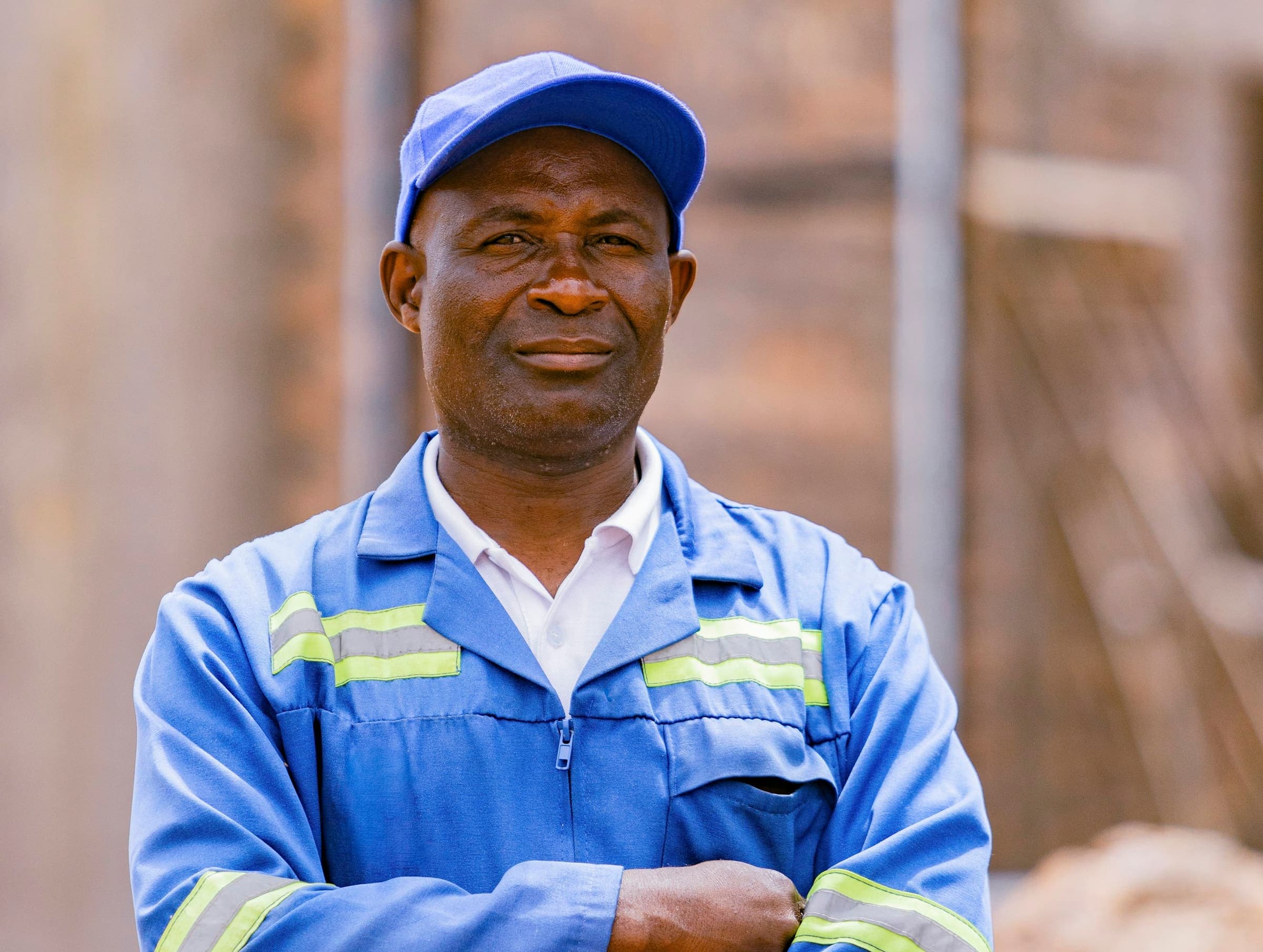 Portrait d’un ouvrier en combinaison bleue réfléchissante et casquette, les bras croisés.